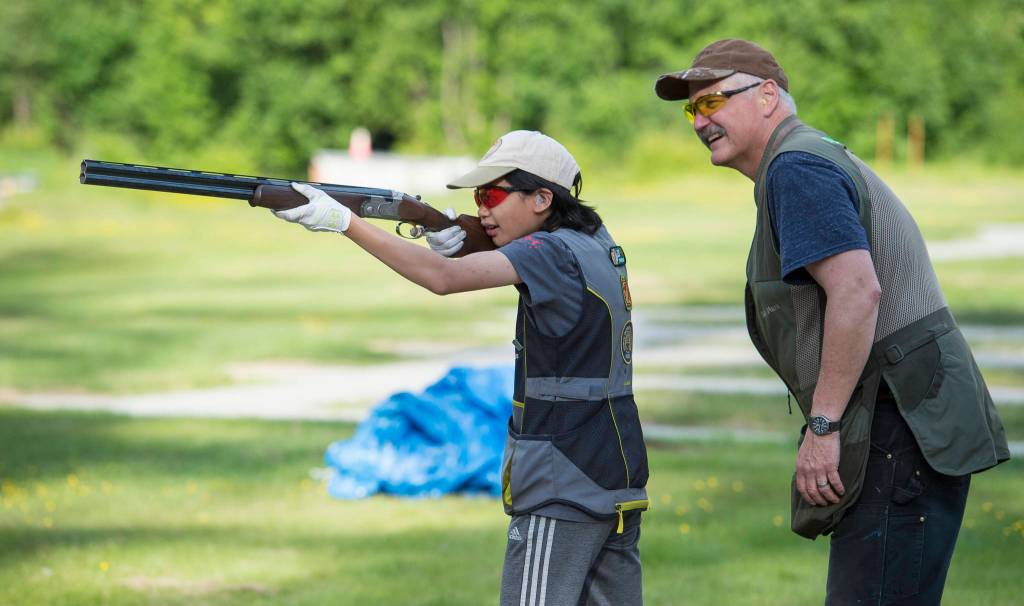 Coach Mark Kappler watches as Mackenzie Lam practices her trap shooting at the Juneau Gun Club on Thursday. (Michael Penn | Juneau Empire)