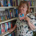 Hearthside Books owner Brenda Weaver holds the Wheres Waldo? sign which will be displayed in downtown Juneau businesses in July to signal to seekers that a six-inch, cardboard Waldo will be hiding in the store. In this July 21 photo, Waldo can be seen standing on the bookshelf. Clara Miller | Capital City Weekly