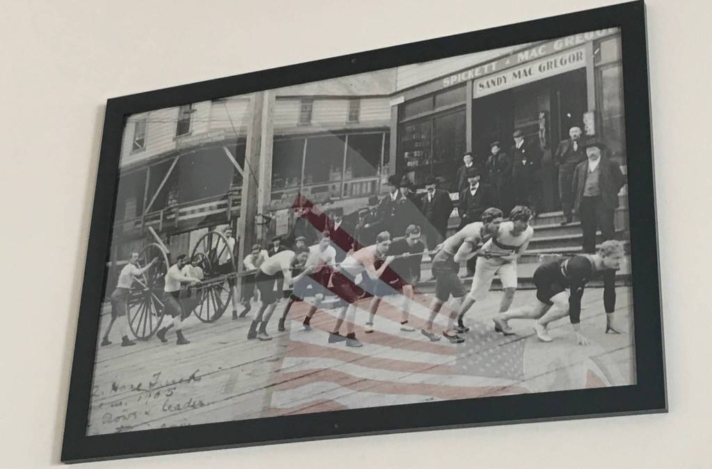 A historic photo dated from 1905 hangs on the wall of the Douglas Fire Station depicting an early Fourth of July hose race. (Alex McCarthy | Juneau Empire)