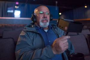 Kenny Solomon-Gross, Vice President and Manager of Gross Alaska Theatres, demonstrates the use of their new closed captioning and assistive listening systems at the 20th Century Theatre in downtown Juneau on Monday, July 16, 2018. The systems are available both downtown and their Glacier Cinemas in the Mendenhall Valley. (Michael Penn | Juneau Empire)