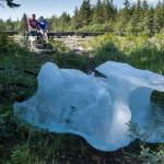 With an iceberg grounded in front of them, Kelly Mercer and her father, Fred Gerle, relax on a bench at the Mendenhall Campground on Friday, July 20, 2018, after Thursdays flood of Mendenhall Lake. (Michael Penn | Juneau Empire)