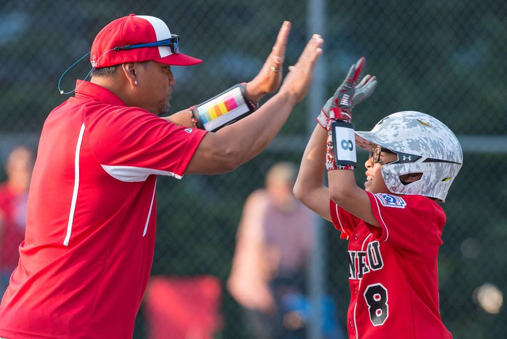 Gastineau Channels Erza Vidal is congratulated on a base hit by coach Randy Quinto against Ketchikan in the eighth inning of the Alaska Major Baseball District 2 Championship Game at Miller Field on Tuesday. (Michael Penn | Juneau Empire)
