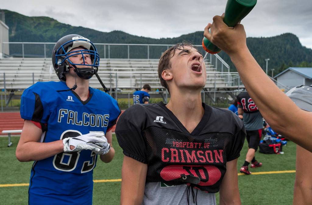 Danny Isaak, of Juneau-Douglas High School, gets a drink as Trey Wilson, of Thunder Mountain High School, waits his turn during Juneau Football practice at Thunder Mountain High School on Thursday, July 26, 2018. (Michael Penn | Juneau Empire)