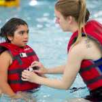 Coast Guard Lieutenant Junior Grade Kat Martorelli helps Harborview third-grader Shawna Boone with her life vest during a water safety class at the Augustus Brown Public Swimming Pool on Friday.