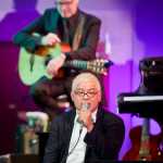 Thomas Lauderdale, leader and founder of Pink Martini, speaks to the sold out audience at the Centennial Hall on Sunday evening. Guitarist Dan Faehnle is in the background.