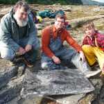 From left to right, USFS Forest Geologist Jim Baichtal, Smithsonian Museum of Natural History Director and paleontologist Kirk Johnson, and geoarchaelogist Ian Putnam pose with a rock slab full of 50 million-year-old fossils.