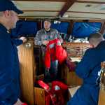 Jacob Miller, center, shows U.S. Coast Guard Petty Officer First Class Ben Stixrud, left, and Petty Officer Second Class Chris Houvener his safety gear on his 41-foot power troller at the Don Statter Memorial Boat Harbor in Auke Bay on Friday.