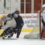Juneau-Douglas High School senior Chase Barnum works the puck under pressure from junior Cahal Morehouse as Crimson Bears' senior goalie Nick Parise guards the corner post during Wednesday morning practice at Treadwell Arena.