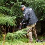 Juneau Police Department Detective Dominic Branson searches a backpack he found in the woods near the Kodzoff Acres Mobile Home Park on Thursday. The pack did not look to be what the department was looking for in relation to the murder of Brandon C. Cook on Tuesday.
