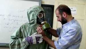 FILE - This image made from an AP video posted on Wednesday, Sept. 18, 2013 shows a volunteer adjusting a students gas mask and protective suit during a session on reacting to a chemical weapons attack, in Aleppo, Syria. The Islamic State group is aggressively pursuing development of chemical weapons, setting up a branch dedicated to research and experiments with the help of scientists from Iraq, Syria and elsewhere in the region, according to Iraqi and U.S. intelligence officials. (AP Photo via AP video, File)