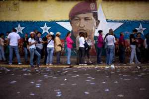 A mural of Venezuelan's late President Hugo Chavez decorates a wall outside a polling station where voters wait to enter during congressional elections in Caracas, Venezuela, Sunday.