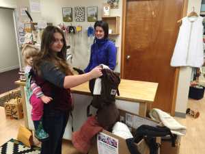 Athena Zellhuber, age 16, Maralie Zellhuber, age three, and Mikaela Levy, owner of Fiddlehead and Ferns, stand with carriers Juneauites are donating to Syrian refugee families in need of them.