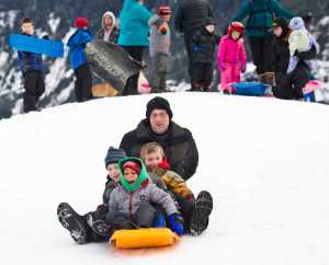 Geoffrey Wyatt sleds with his son, Lucas, 5, Orion Paden, 5, and Momar Diouf, 3, in front of the Mendenhall Glacier Visitors Center on Monday.