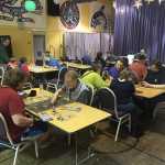 Main hall at Platypus-Con 2015 at the Juneau Arts and Culture Center. Pictured are people using games from the lending library with some players teaching new players, or new players being taught by Platypus-Con staff.