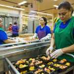 In this photo taken Jan. 13, from left, Jackie Garcia, Chieu Montgomery, and Carmen Sanchez prepare meals of whole grain chicken nuggets and maple sweet potato cubes at the Anchorage School District nutrition center in Anchorage.