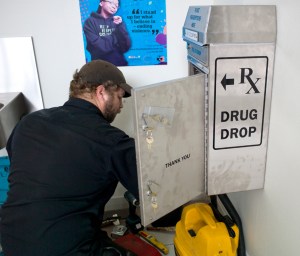 Sergei Morosan of the CBJ buidling maintanance department installs a new prescription drug drop box in the lobby of the Juneau Police Department on Tuesday, July 7, 2015.