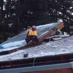 The workers carefully install roofing and flashing around the tribal house's "smokehole" skylight feature last year.