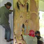 The Kaagwaantaan House post is raised for display at  Xúna Shuká Hit (Glacier Bay Tribal House). At left is carver Owen James.