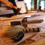 From front to back, an adze blade guard, a straw broom, and an adze rest on the 28-foot cedar log that will become a canoe as carvers work. (National Park Service | Erin Fulton)