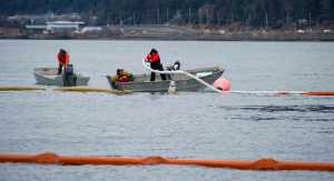 Absorbent booms are placed as the barge-crane Brightwater lifts the sunken 96-foot tugboat Challenger in Gastineau Channel on Sunday. Once the tug is dewatered, patched and stabilized, the WWII era vessel will be towed to the AJ Cruise Ship Dock for further work.