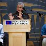 Edna MacLean, Commissioner of Iñupiat History, Language, and Culture for the North Slope Borough, speaks at the Alaska Language Summit at the Walter Soboleff Building on Tuesday. Rep. Jonathan Kreiss-Tomkins, D-Sitka, left, and X̱unei Lance Twitchell, Assistant Professor of Alaska Native Languages at the University of Alaska Southeast, listen on stage in the Shuká Hit Clan House.