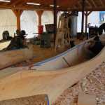 At left, Steven Price works on a small dugout to be displayed in Skagway, while carvers James (Gooch Éesh) Hart, Zack (Tlél Tooch Tláa.aa) James, and Wayne Price work on the first of two 40-foot spruce dugout canoes. All three apprentice carvers are volunteering their time, working ten hours a day, seven days a week for about nine months.