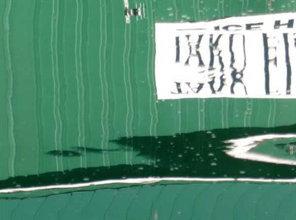 The side of a downtown icehouse reflects in harbor waters on a windy day, creating a wavy abstract. Photo by Denise Carroll.