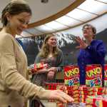 IMAGE DISTRIBUTED FOR MATTEL, UNO - Jess Brown, left, picks up a deck of UNO cards and an UNO postcard as Juneau Deputy City Manager Mila Cosgrove, right, and her daughter, Natalie, look on in the city's Assembly Chambers on Friday, April 1, 2016. As part of an April Fools' promotion, the city of Juneau and Mattel announced a renaming of Juneau to UNO. (Michael Penn/AP Images for Mattel, UNO)