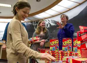 IMAGE DISTRIBUTED FOR MATTEL, UNO - Jess Brown, left, picks up a deck of UNO cards and an UNO postcard as Juneau Deputy City Manager Mila Cosgrove, right, and her daughter, Natalie, look on in the city's Assembly Chambers on Friday, April 1, 2016. As part of an April Fools' promotion, the city of Juneau and Mattel announced a renaming of Juneau to UNO. (Michael Penn/AP Images for Mattel, UNO)
