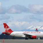 A Virgin America plane taxis past an Alaska Airlines plane waiting at a gate, Monday, April 4, 2016, at Seattle-Tacoma International Airport in Seattle. Alaska Airlines' parent company announced Monday that it will pay $2.6 billion to buy the Richard Branson-inspired, California-based Virgin America. (AP Photo/Ted S. Warren)