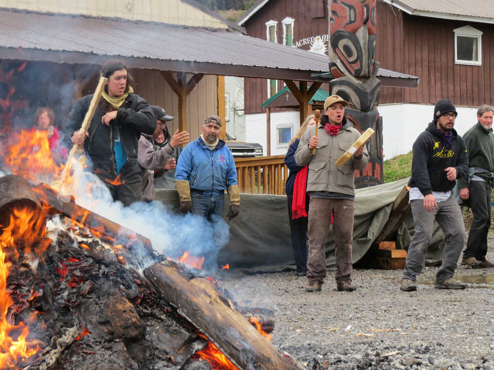 In the foreground, from left, carvers Zack James, Ted Hart and James Hart dance as Ted Hart drums. Zack James and James Hart are in Hoonah from Haines for several months to carve two forty-foot spruce canoes for the ceremonial return of the Huna Tlingit to Glacier Bay; Ted Hart came down with his family for the week to help out. In the foreground is the fire on which they're heating the rocks to steam the canoe, covered with a tarp in the background.