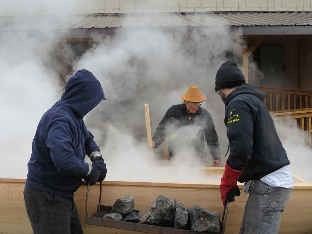 Don Bolton, left, and James Hart carry fire-heated rocks to the canoe for steaming as lead carver Wayne Price evaluates the expansion's progress.