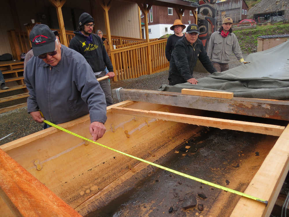 Melvin Williams measures the canoe. It expanded from around 37 inches at its widest point to around 59 inches before it developed a crack. Carvers are repairing the crack before they resume steaming. At his right are James Hart, Cherri Price, Wayne Price and Ted Hart. At the bottom of the canoe is ash from the heated rocks, which community members later washed out.