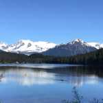 To the right, Dayna Deuter paddleson Auke Lake in her rowing shell and passes UAS students to the left.