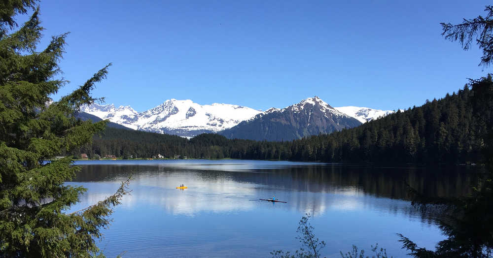 To the right, Dayna Deuter paddleson Auke Lake in her rowing shell and passes UAS students to the left.