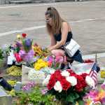 Vanessa Buzgheia, of Louisville, Ky., sets up flowers that were knocked over by the wind at a memorial to Muhammad Ali at the Muhammad Ali Center, Saturday, June 4, 2016 in Louisville Ky. Ali, the magnificent heavyweight champion whose fast fists and irrepressible personality transcended sports and captivated the world, has died according to a statement released by his family Friday, June 3. He was 74. (AP Photo/Timothy D. Easley)