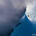 A sharp ridge emerges dramatically from the rolling clouds.