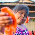 Ella Mooney holds up a small sockeye filet while learning from her aunts how to smoke salmon on a warm summer afternoon in Hydaburg. Photo by Bethany Goodrich.