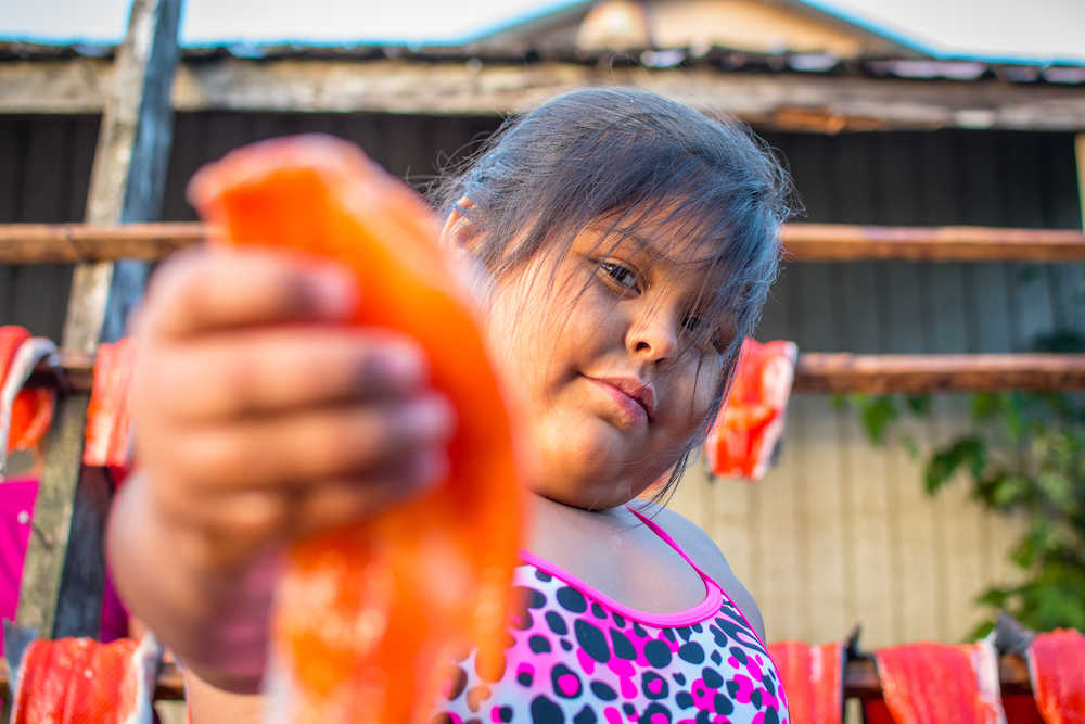 Ella Mooney holds up a small sockeye filet while learning from her aunts how to smoke salmon on a warm summer afternoon in Hydaburg. Photo by Bethany Goodrich.