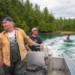 Sam Mooney speeds the skiff around a school of sockeye, hoping to trap salmon in the beach seine attached to the blue dingy. Photo by Bethany Goodrich.