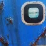 Rusty pockmarks on a steel boat's surface with a reflection of the entire boat in the porthole.  Cape Cod, July 2016.