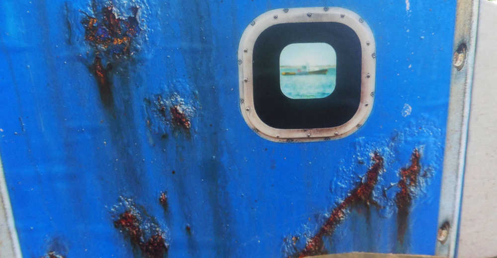 Rusty pockmarks on a steel boat's surface with a reflection of the entire boat in the porthole.  Cape Cod, July 2016.