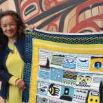 Master weaver Clarissa Rizal holds up one end of the "Weavers Across the Water" Chilkat and Ravenstail blanket. Forty Ravenstail and Chilkat weavers contributed a square measuring around five inches by five inches. Rizal wove the border around the robe, a pattern called "Mating Loons," and is working them all into a robe that will get its first use during the dedication ceremony for Xunaa Shuka Hit, the Glacier Bay tribal house.