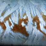 Rust on a guardrail resembles snow-covered mountainous terrain.