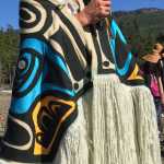 Standing Chief Son-i-Hat, John McAllister, welcomes and grants permission to canoes to land on the beach before Naay i'Waans.