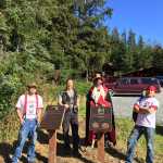 From left to right, restoration crew apprentice carver Wooshdeiteitxh (Justin Henricks), lead carver Gitajang (Glenn "Stormy" Hamar), apprentice carver Nang K'adangaas (Eric Hamar), and apprentice carver St'igiinii (Harley Holter) stand behind the plaques honoring their and past carvers' contributions to the restoration of Náay í'Waans.