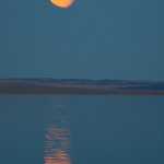 Not to be outdone by the sun, the nearly full moon rises like a giant orange saucer over Simpson Strait.
