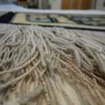 Newer fringe, added to the Chilkat blanket by Anna Brown Ehlers, noticeable by its light color and newer bark can be seen interspersed with the older fringe.