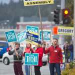 Assembly candidate Norton Gregory, right, waves his sign to commuters on their way home at the corner of 10th Street and Egan Drive on the Municipal Election eve on Monday.