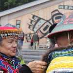 Weaver Clarissa Rizal adjusts the "Weavers Across the Waters" robe on carver Wayne Price in front of Xunaa Shuká Hít. Both artists are masters in their respective fields. Price was the first to wear and dance with the robe, woven by 44 weavers from up and down the Pacific Northwest.